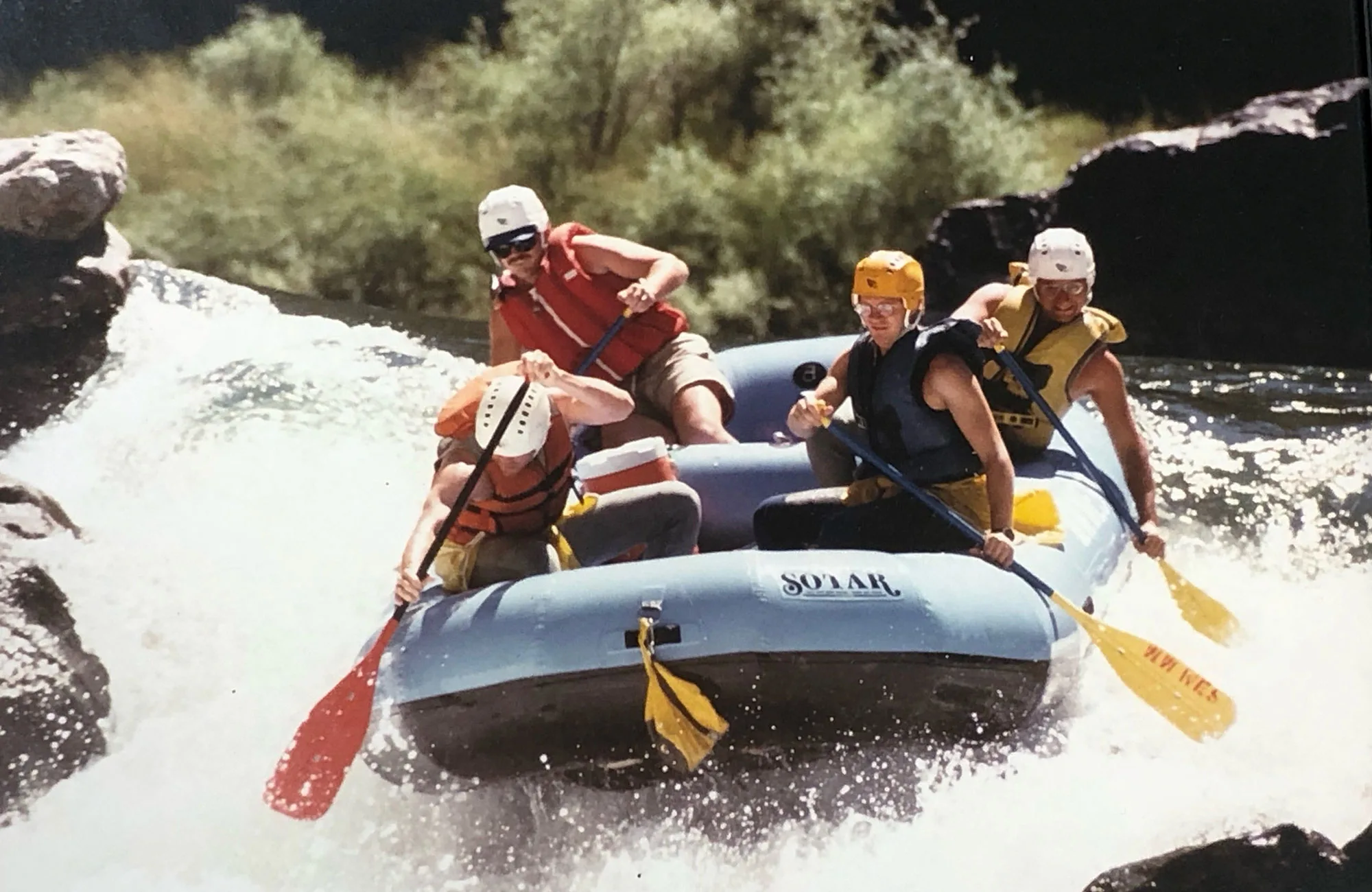 The friends are shown here whitewater rafting in 1986 on the Trinity River in California. Front of the raft, left to right: Robert Thieke and Michael Drews; back of raft, left to right: rafting guide and Frederick Rozner.